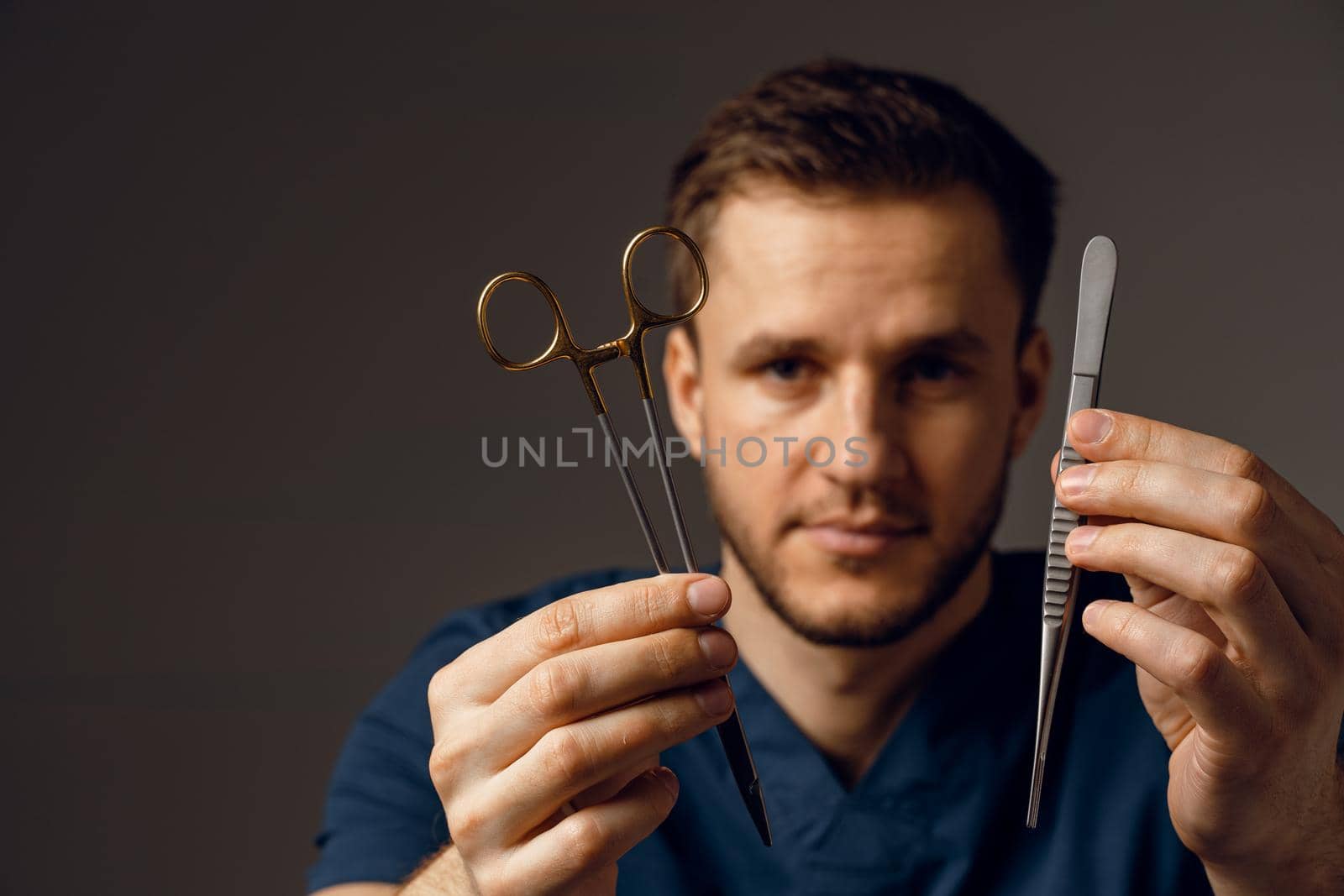 Handsome doctor with surgical scissors and needle holder. Confident man holding medical equipment in hands by Rabizo