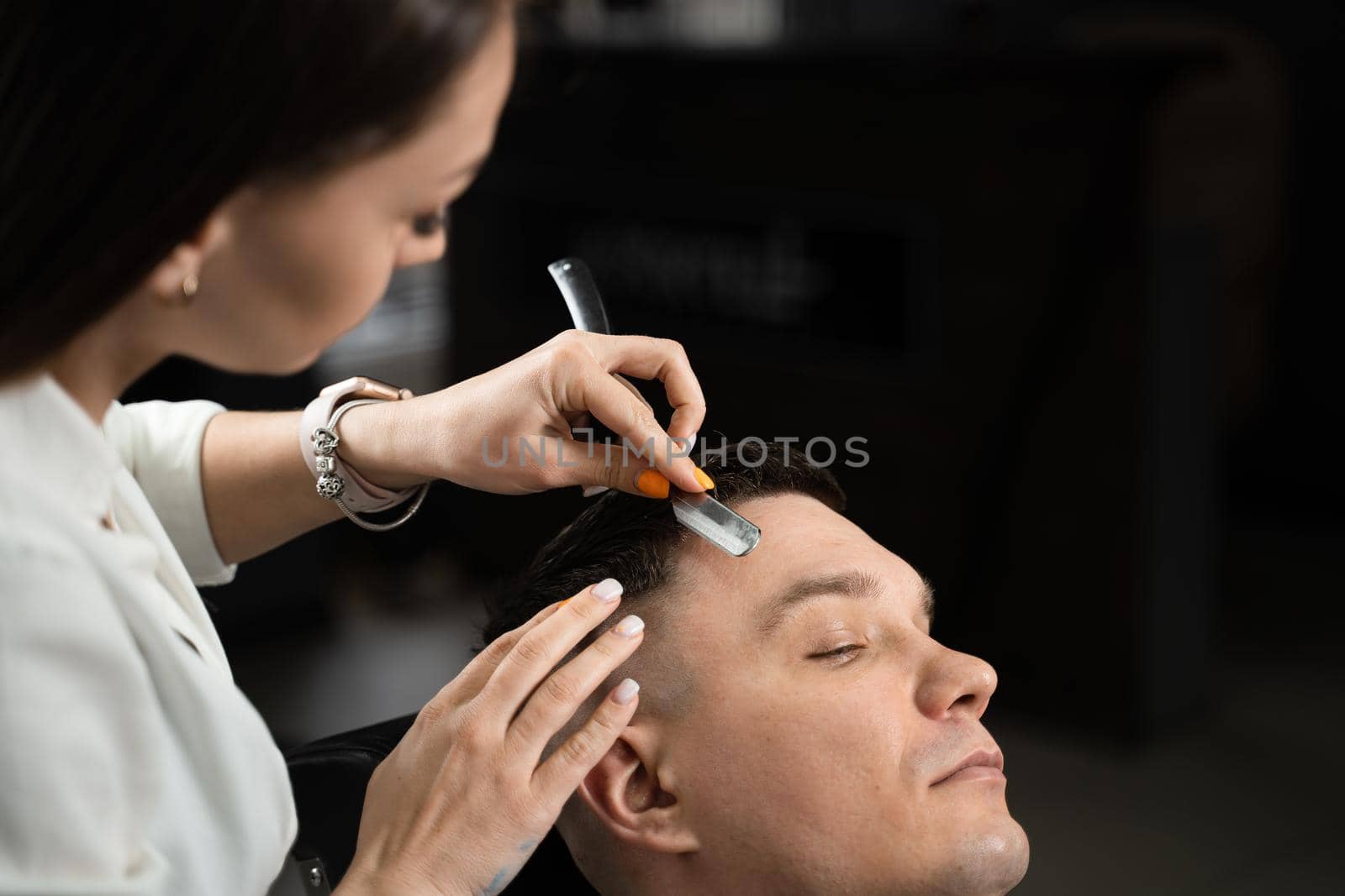 Straight razor cut man hair in barbershop. Attractive woman barber making hairstyle for handsome man. by Rabizo