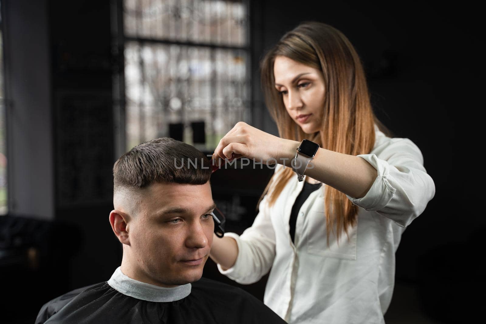 Woman barber making hairstyle in barbershop using clipper. Hairdresser cutting hair of handsome man