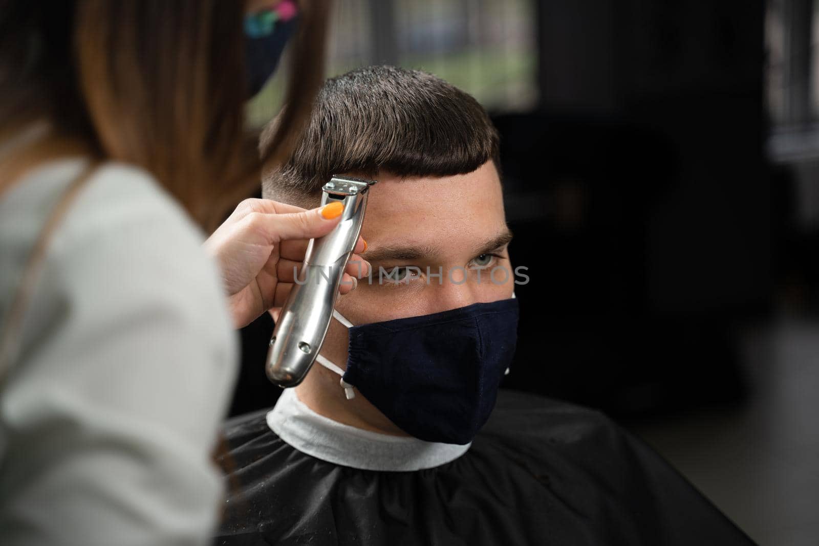 Barbershop customer in medical mask for protection against coronavirus covid-19. Making hairstyle for handsome man