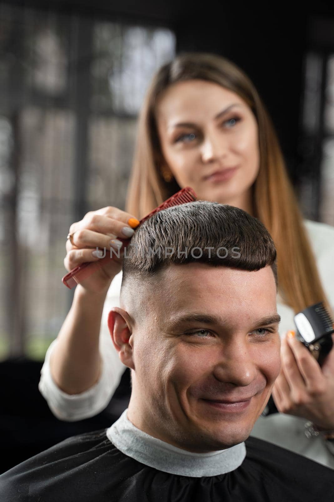 Woman barber making hairstyle in barbershop using clipper. Hairdresser cutting hair of handsome man