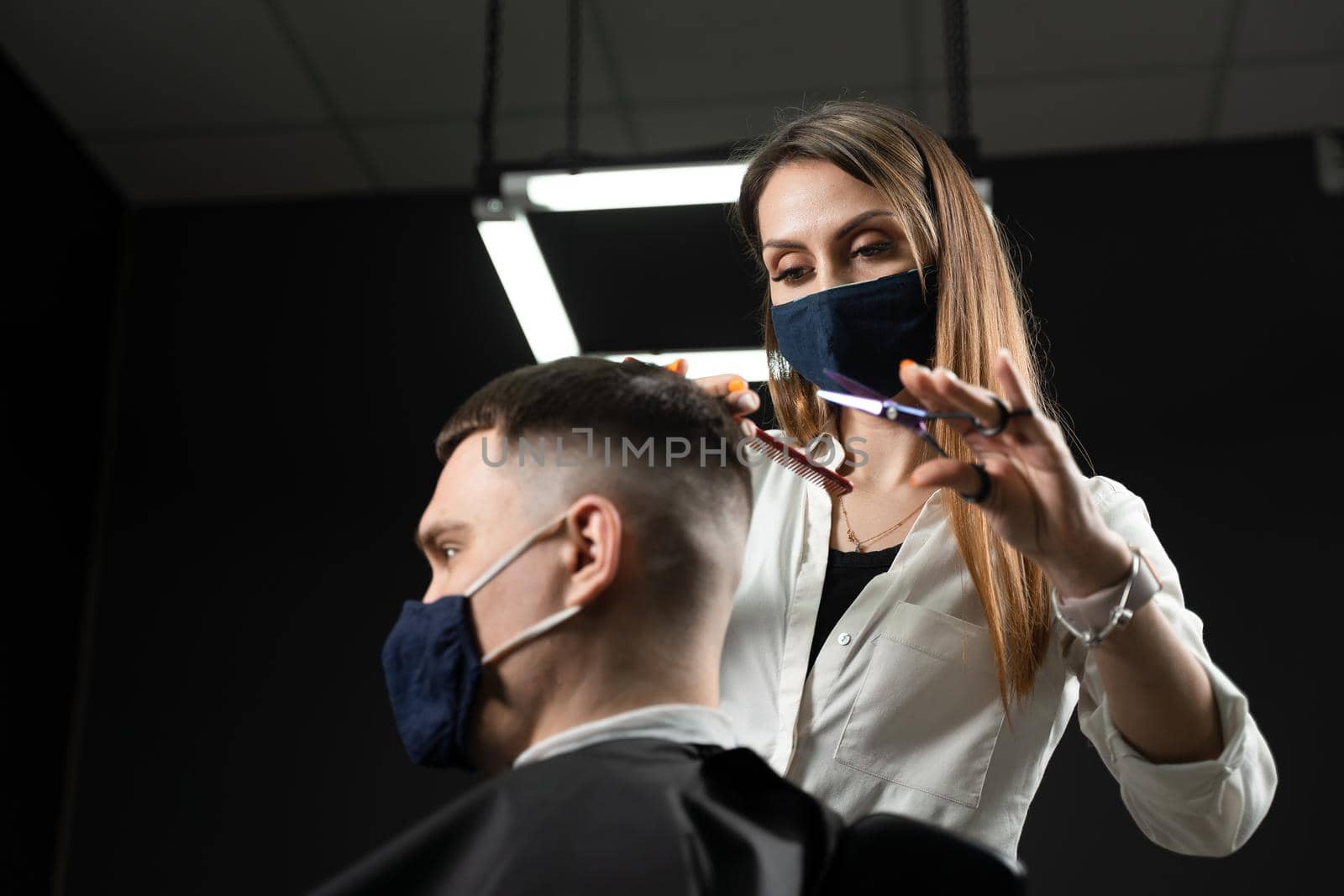 Barbershop service at coronavirus covid-19 period. Woman barber making hair for handsome man. Using mask