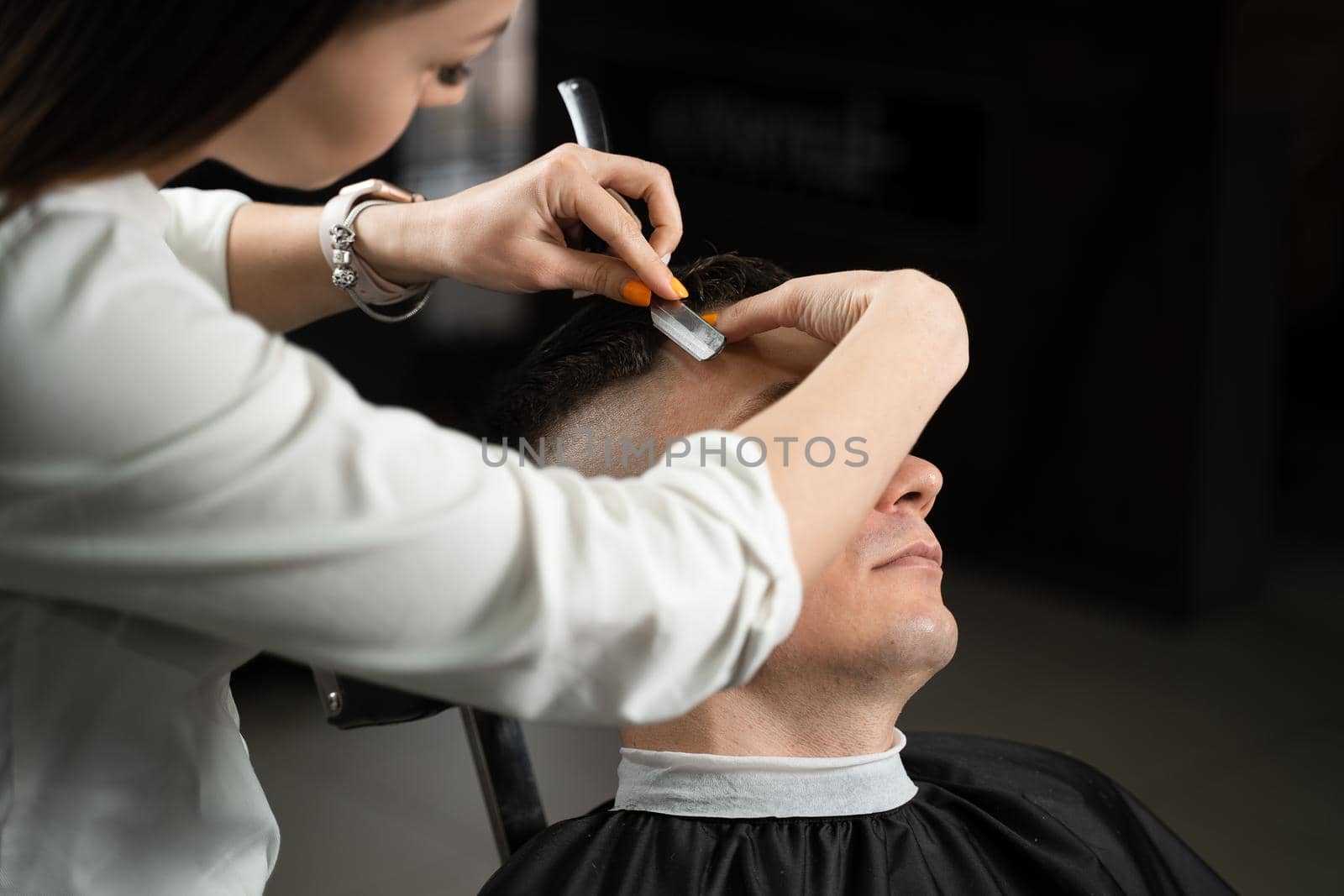 Straight razor cut man hair in barbershop. Attractive woman barber making hairstyle for handsome man. by Rabizo