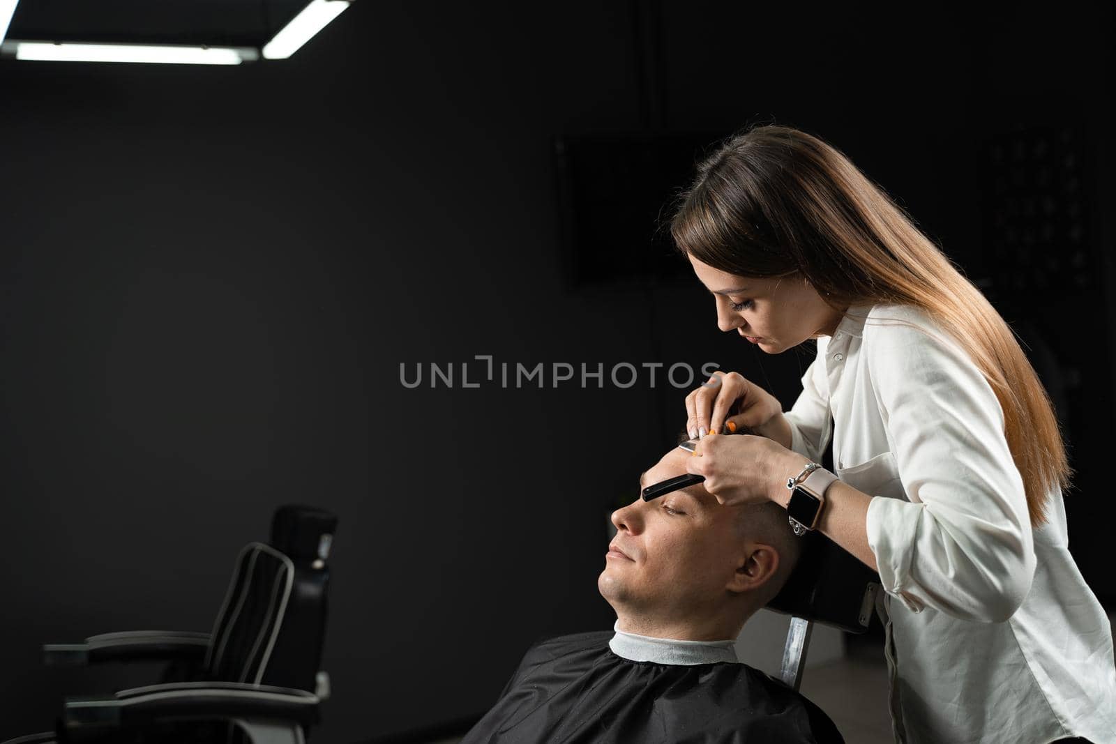 Straight razor cut man hair in barbershop. Attractive woman barber making hairstyle for handsome man. by Rabizo