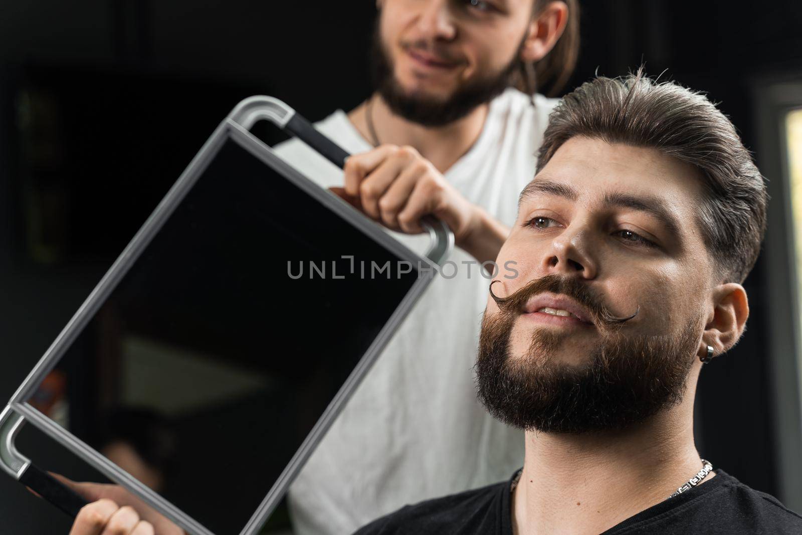 Barber with dreadlocks showing result of low fade machine hair and beard cut for bearded man in barbershop. Hairstyle with a smooth transition