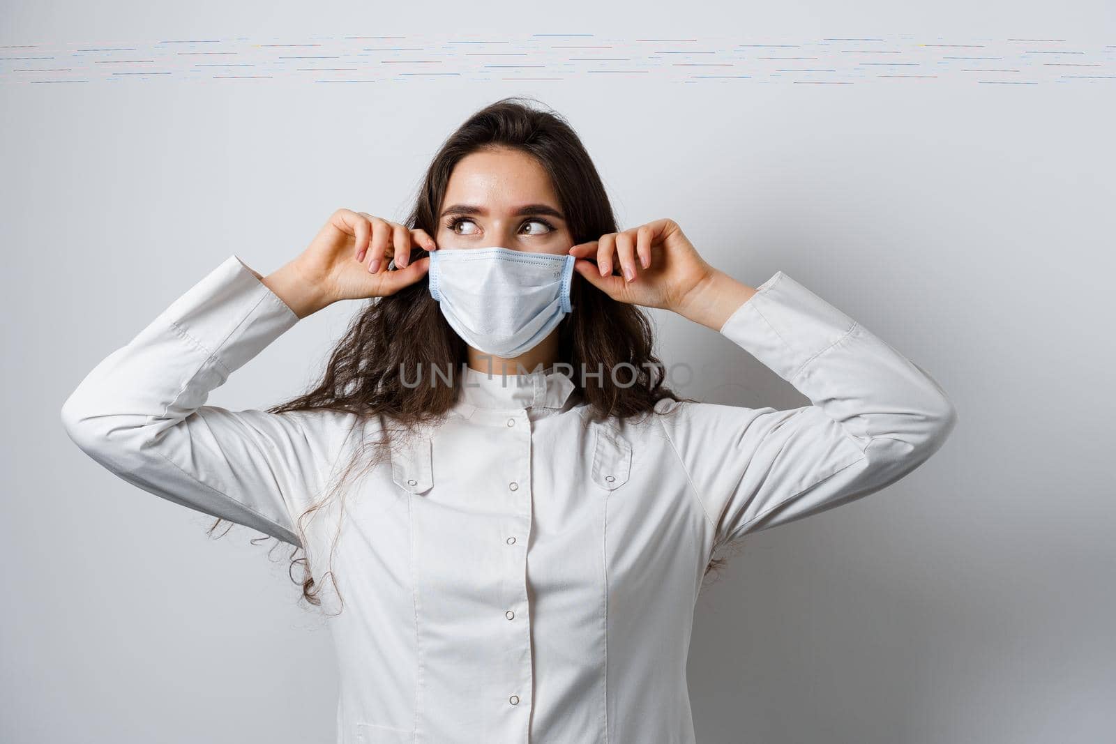 Doctor wearing medical mask on white background. Young attractive woman in medical robe. Quarantine coronavirus covid-19 trends.