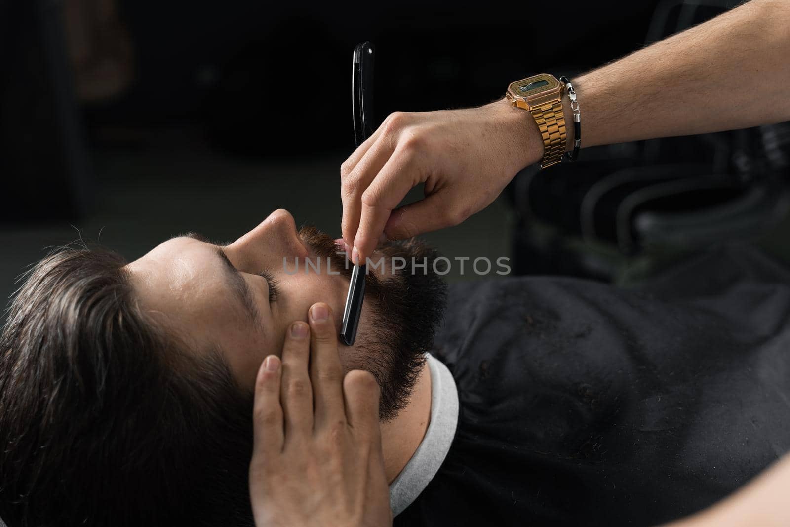 Straight razor cut mans beard in barbershop. Barber man making hairstyle for handsome man