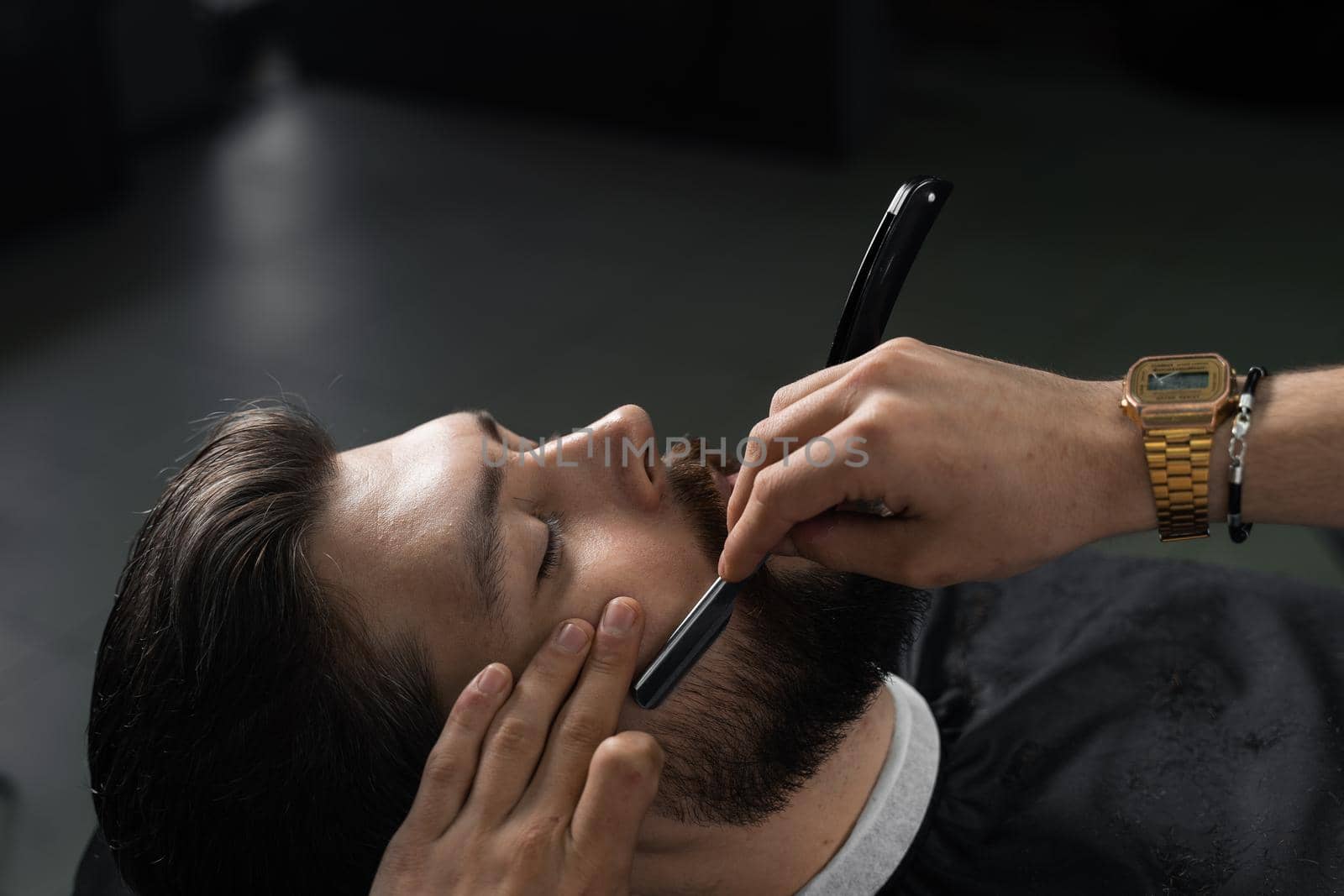 Straight razor cut mans beard in barbershop. Barber man making hairstyle for handsome man