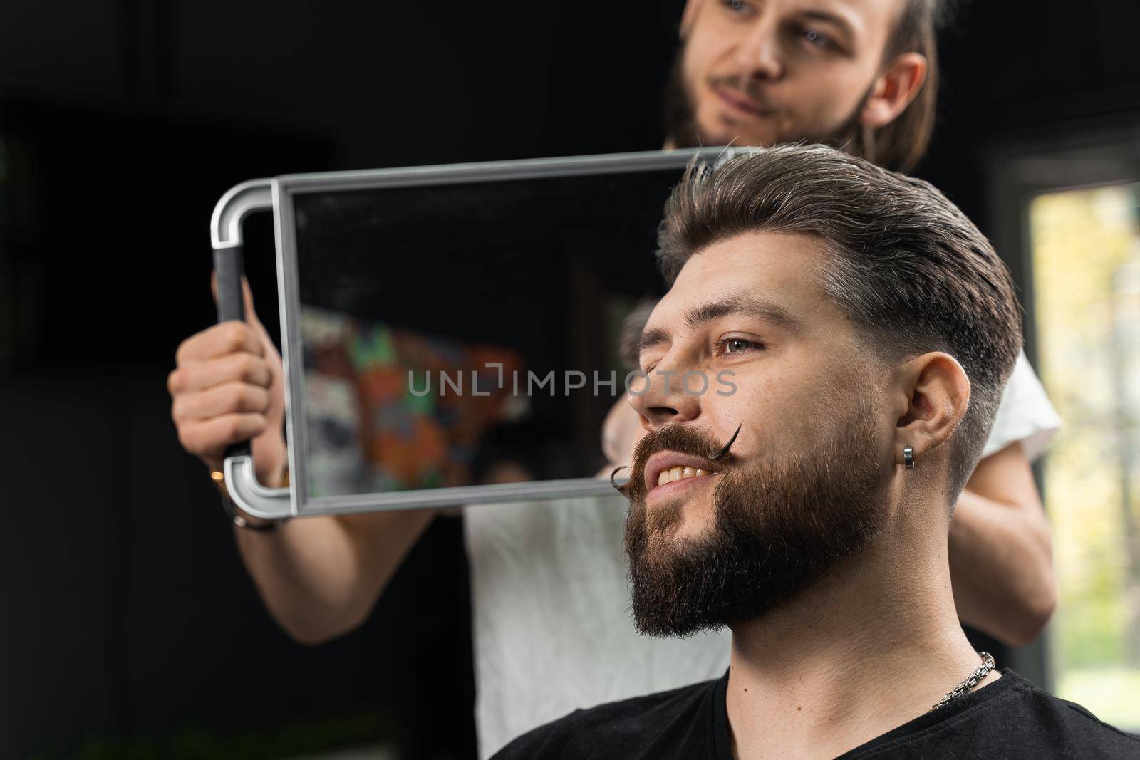 Barber with dreadlocks showing result of low fade machine hair and beard cut for bearded man in barbershop. Hairstyle with a smooth transition