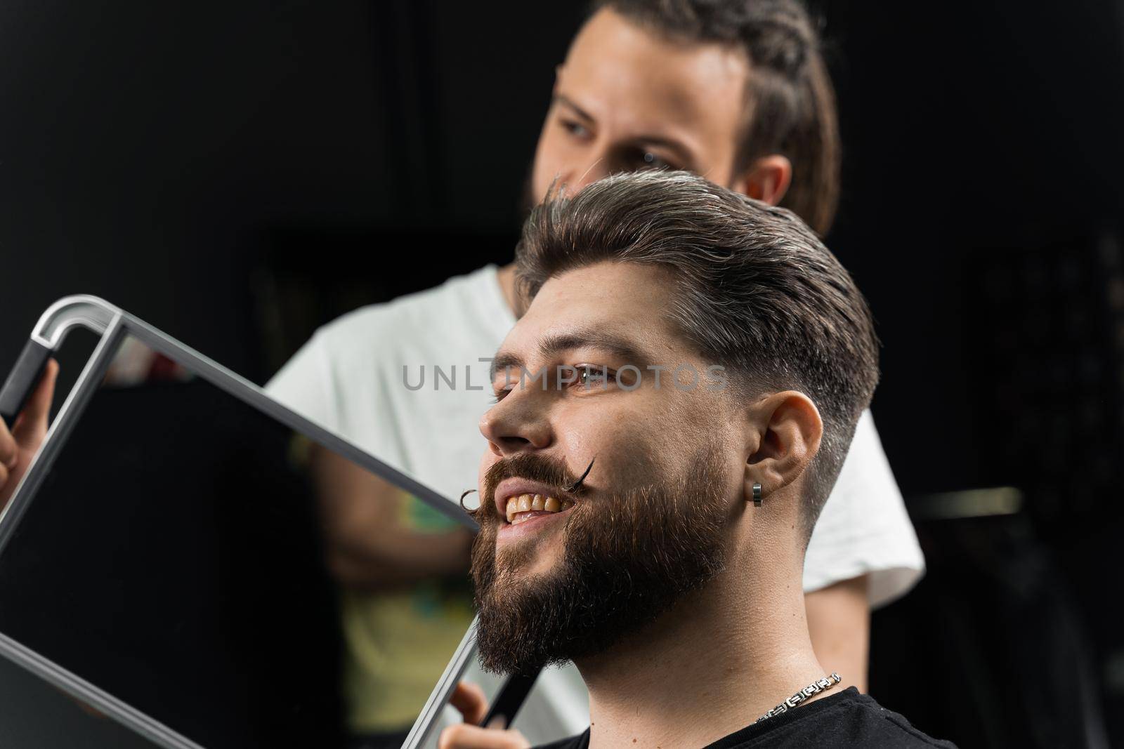 Barber with dreadlocks showing result of low fade machine hair and beard cut for bearded man in barbershop. Hairstyle with a smooth transition