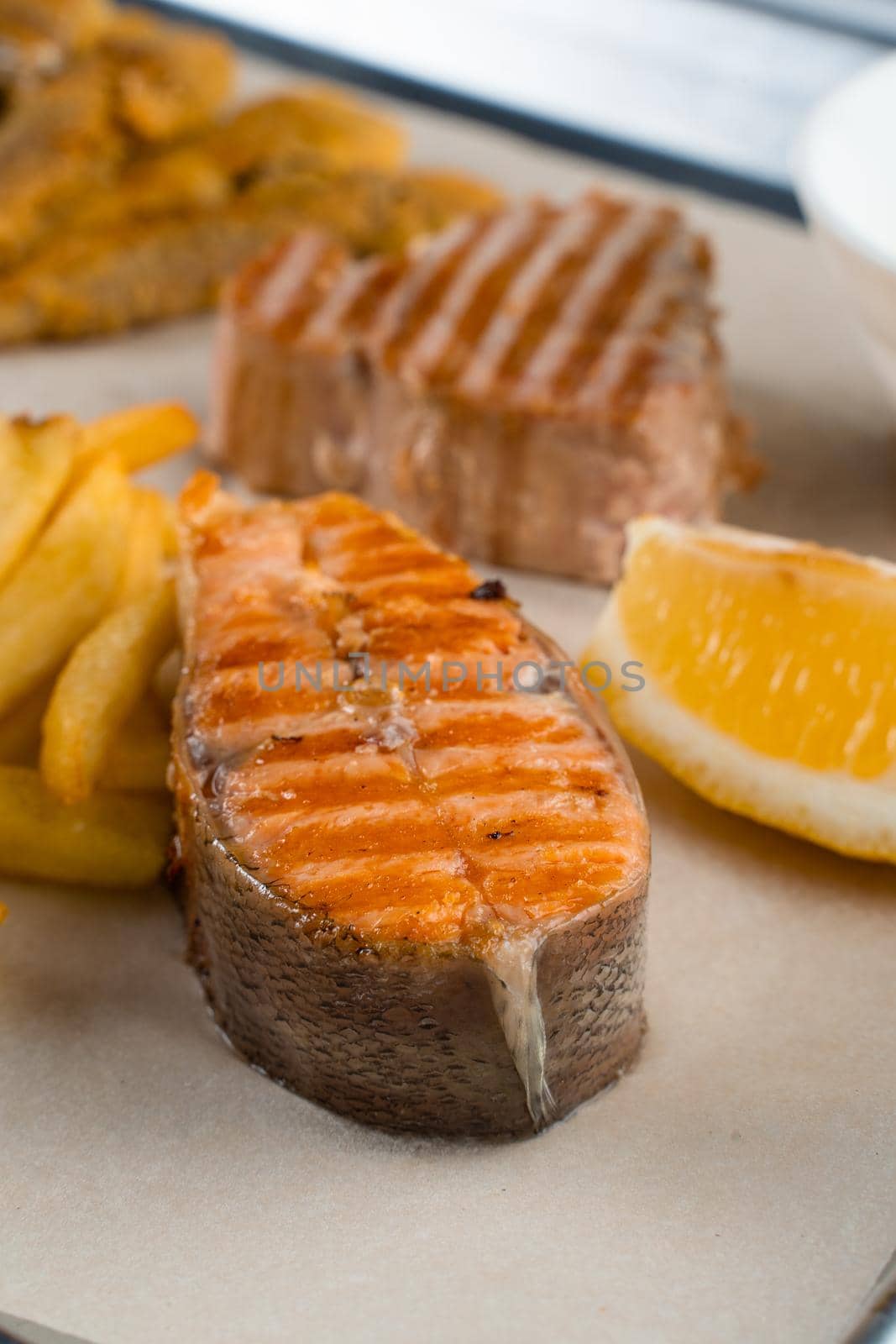 Grilled salmon steak with lemon and fries on light background