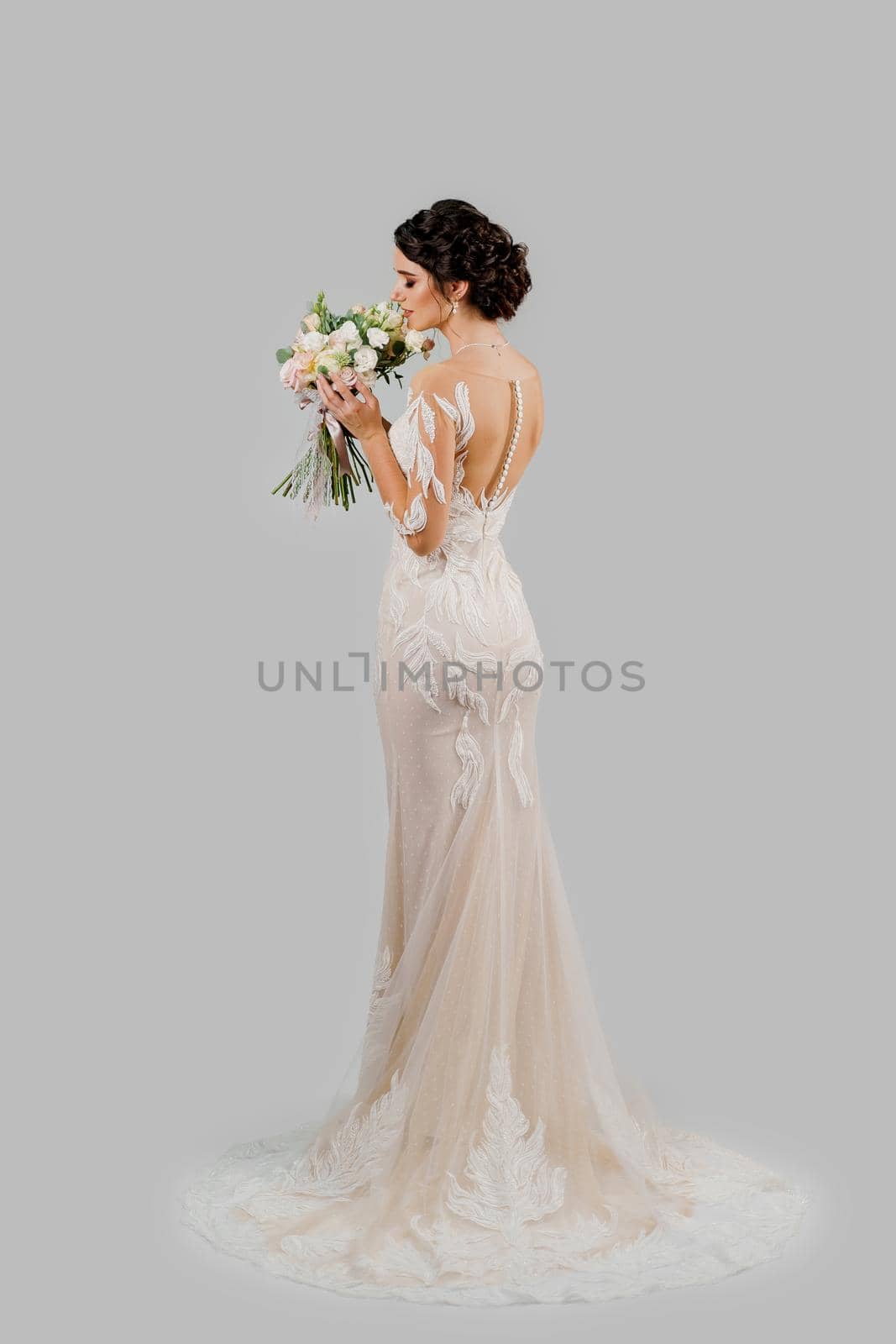 Bride in wedding dress holds and sniff bouqet in studio on blank background. Attractive girl portrait. Vertical photo for advert in social networks.