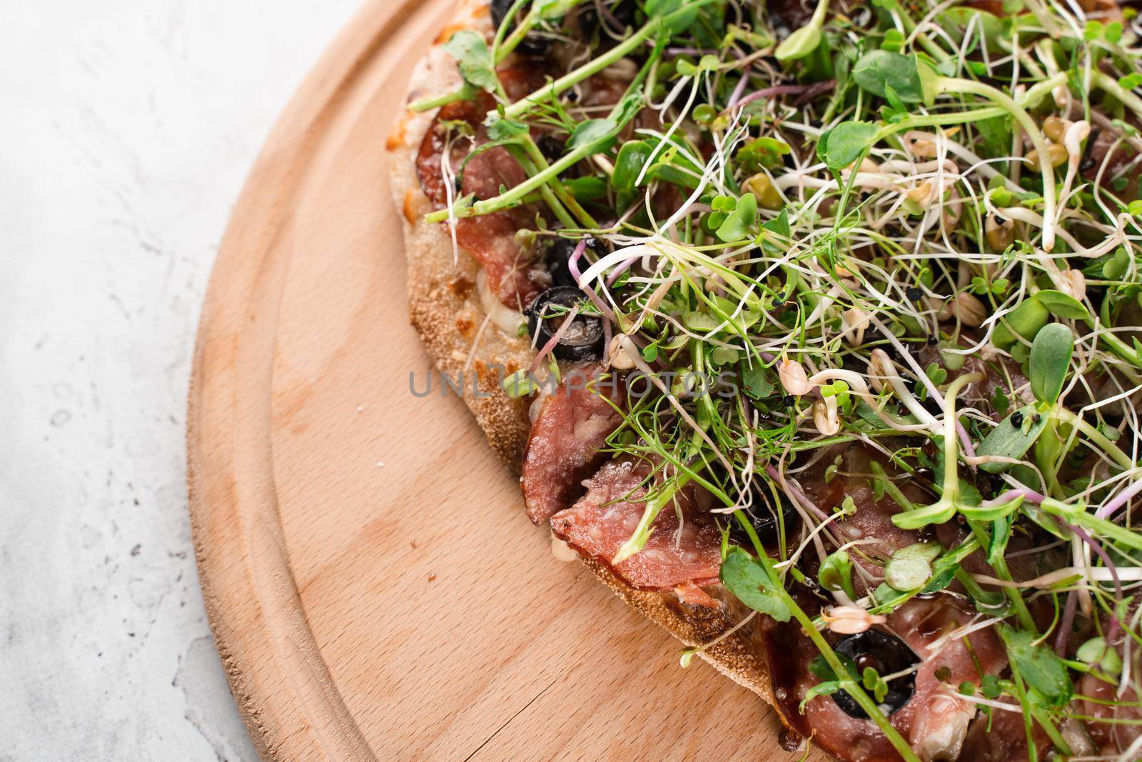 Pinsa romana with salami, cheese, mushrooms, decorated with microgreens on wooden boardon white background