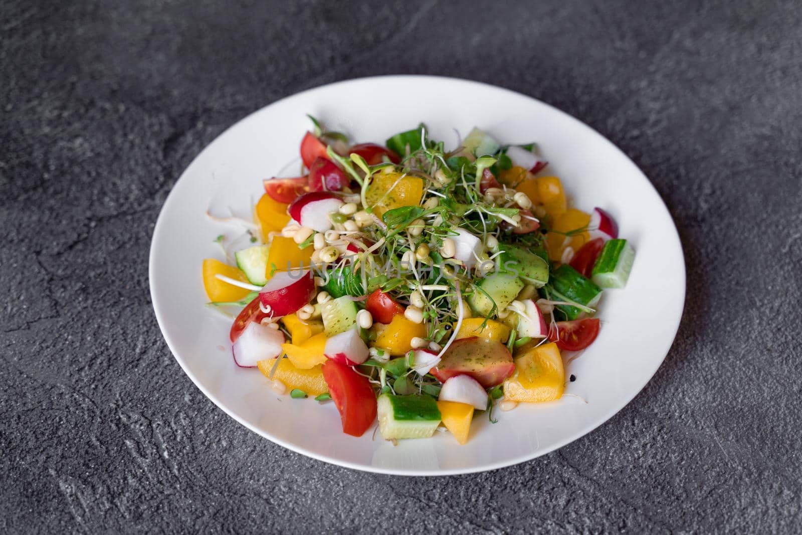 Wheat germ salad, tomatoes, peppers, radish, cucumber, olive oil. Vegetable salad on white plate on gray background.