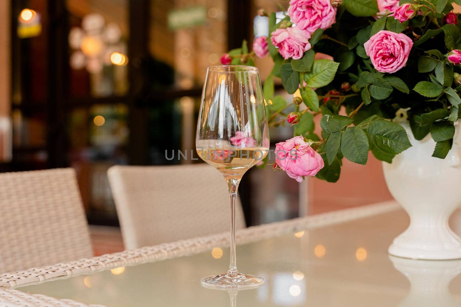 Glass of white wine against the background of bouquet roses in white vase on light table