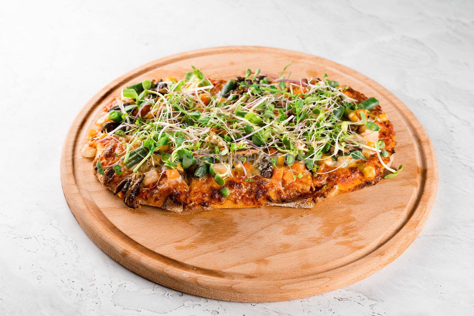 Vegan pinsa romana with mushrooms, asparagus, corn, peas, carrots, cheese and sauce, garnished with microgreens on wooden board