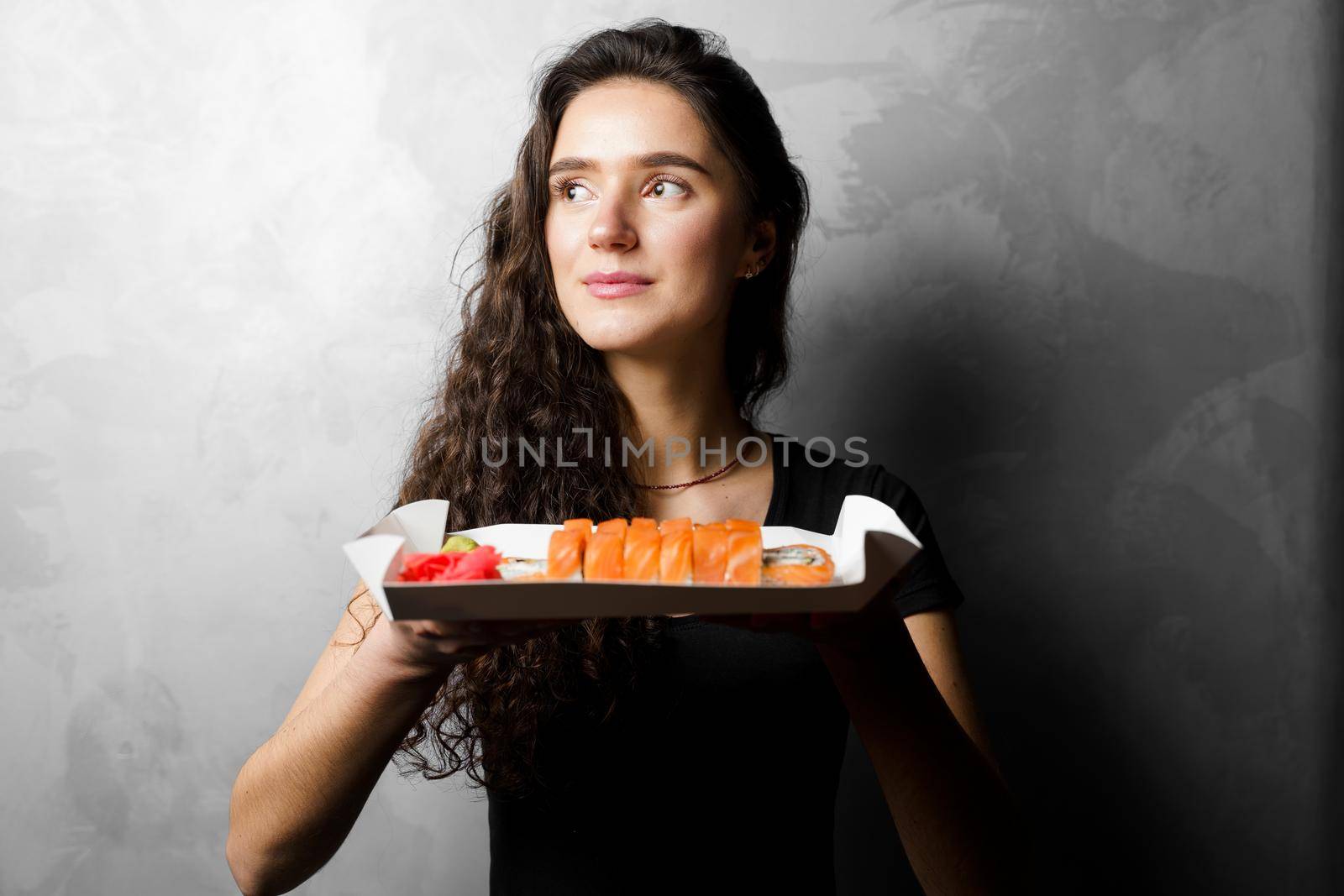 Girl holding philadelphia rolls in a paper box on gray background. Sushi, food delivery