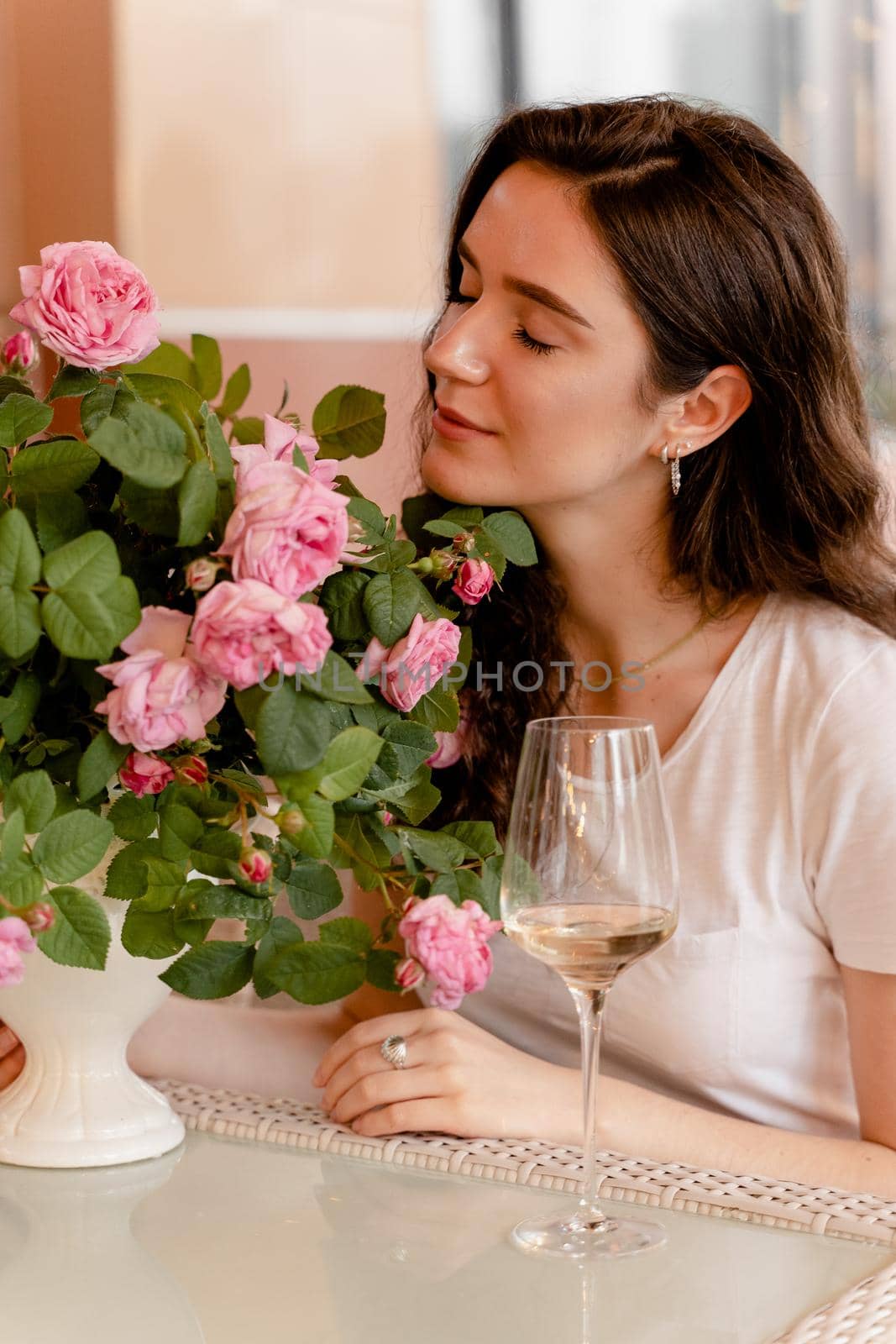 Dreaming woman with glass of alcoholic white wine in cafe in summer terrace and bouquet of roses on the table