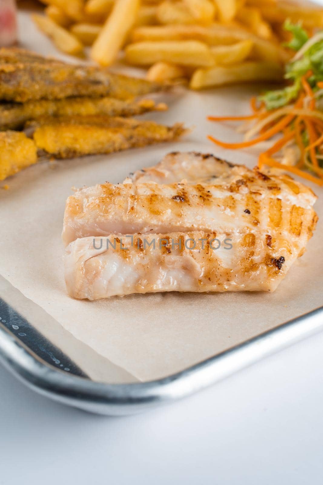 Grilled fillet white fish on background of salad, french fries, on on metal plate.