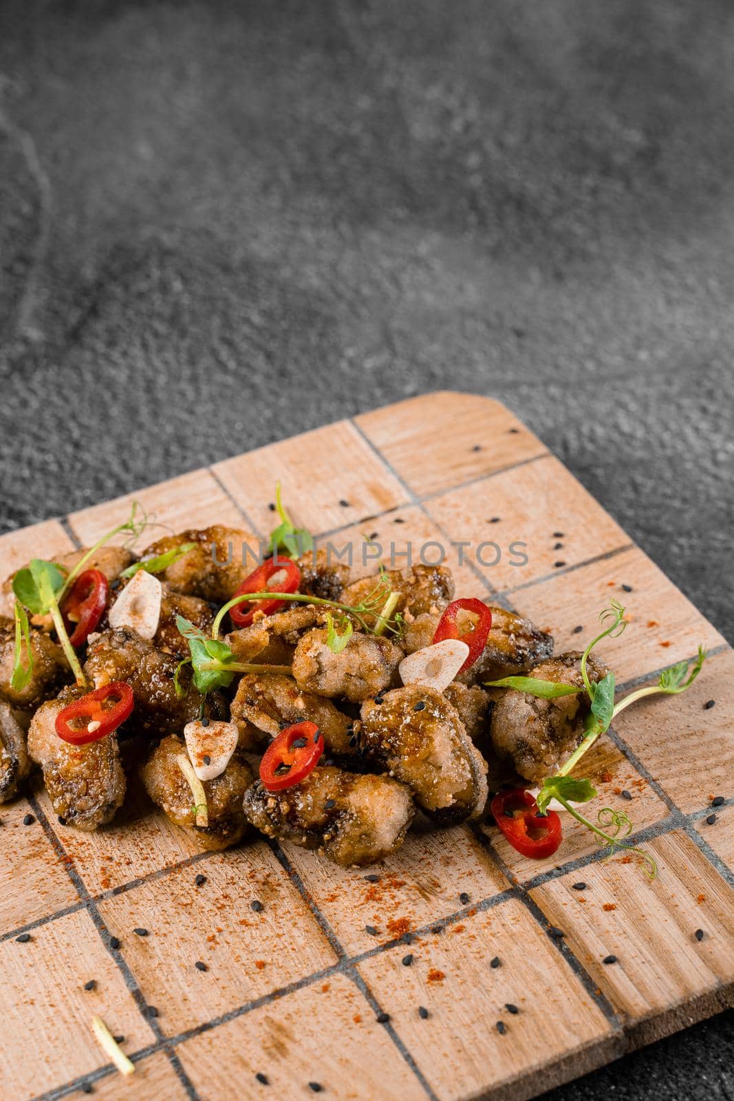 Fried mussels with chili, garlic, sesame, herbs, on square wooden board on gray background