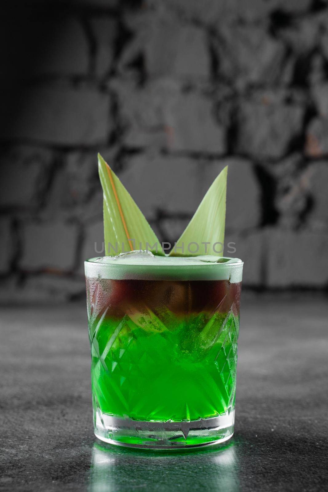 Green layered cocktail decorated with bamboo leaves on a gray background. by Rabizo