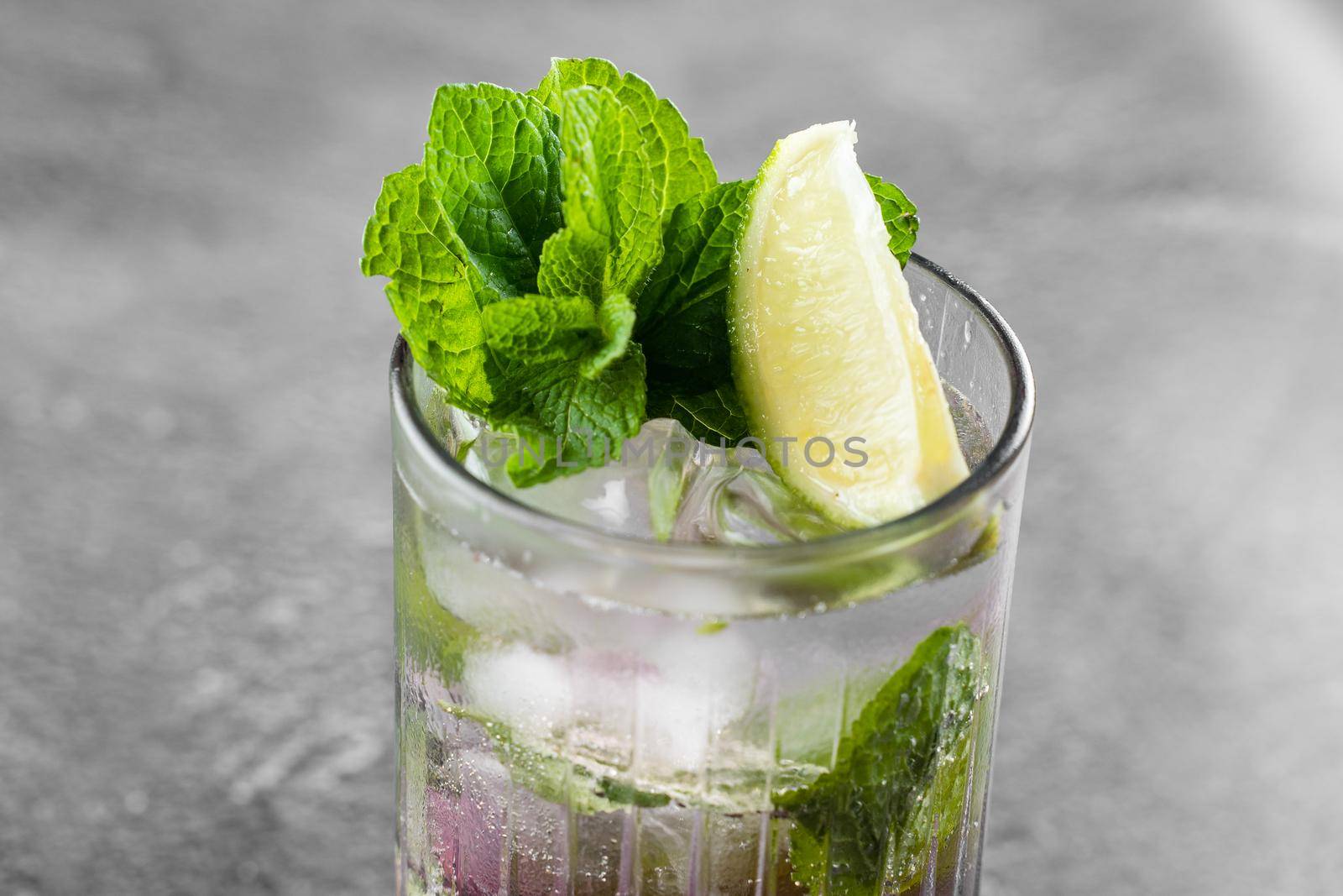 Cocktail with tonic, currant syrup, lime, mint, ice in tall glass on gray background. Puff cold drink with blueberries. by Rabizo