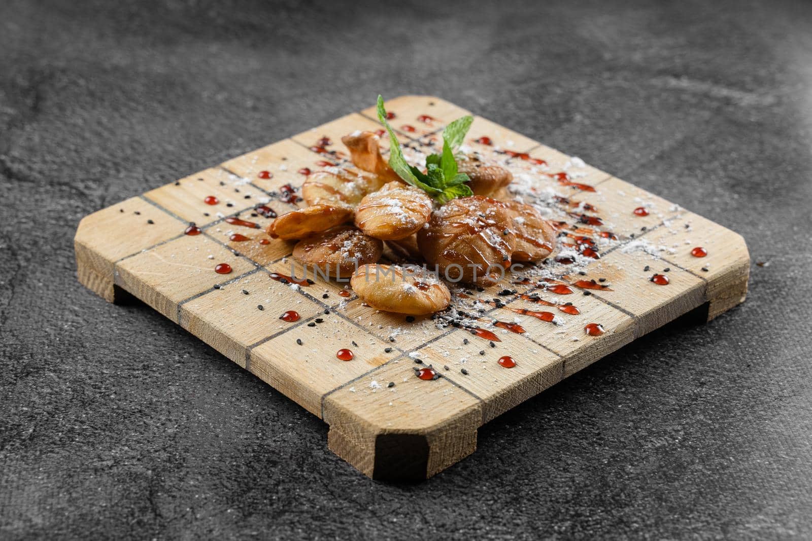 Rice crackers with maple syrup and powdered sugar garnished with mint on square wooden board on gray background. Deep-fried biscuits. by Rabizo