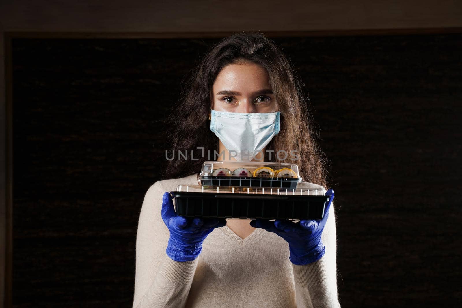 Girl with sushi. Food courier in medical mask. Delivery at quarantine coronavirus covid-19. Young woman holding 2 sushi boxes in hands using gloves