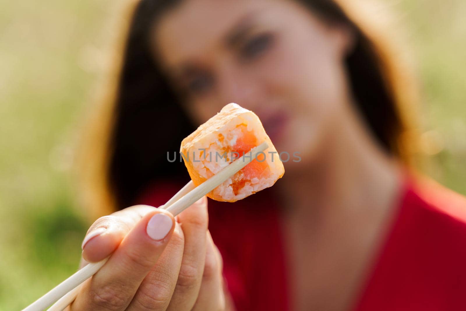 Close-up one sushi. Attractive girl holds sushi with chopsticks in hands and gives to you. Courier delivered sushi set for pretty woman. Black box with sushi, wasabi, ginger.