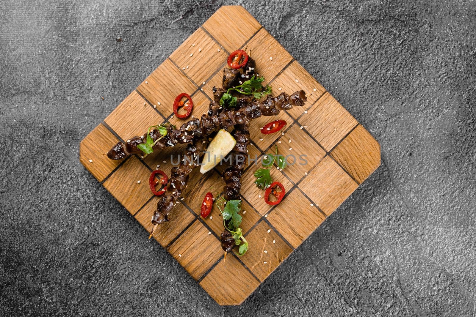 Grilled chicken hearts with lime on wooden skewer, garnished with chili, cilantro, sesame on gray background. by Rabizo