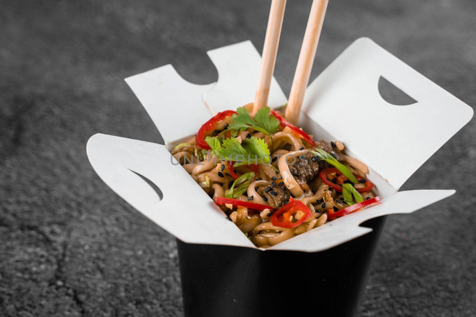 Wok in box spicy noodles in black food container. Fast food delivery service. Takeaway chinese street meal. by Rabizo