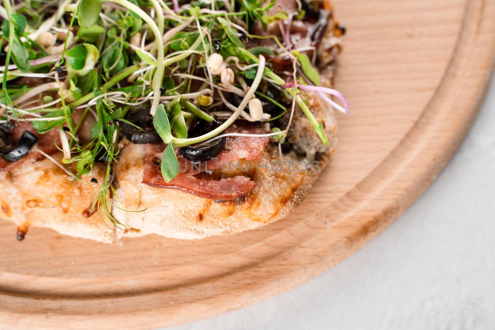 Pinsa romana with salami, cheese, mushrooms, decorated with microgreens on wooden boardon white background