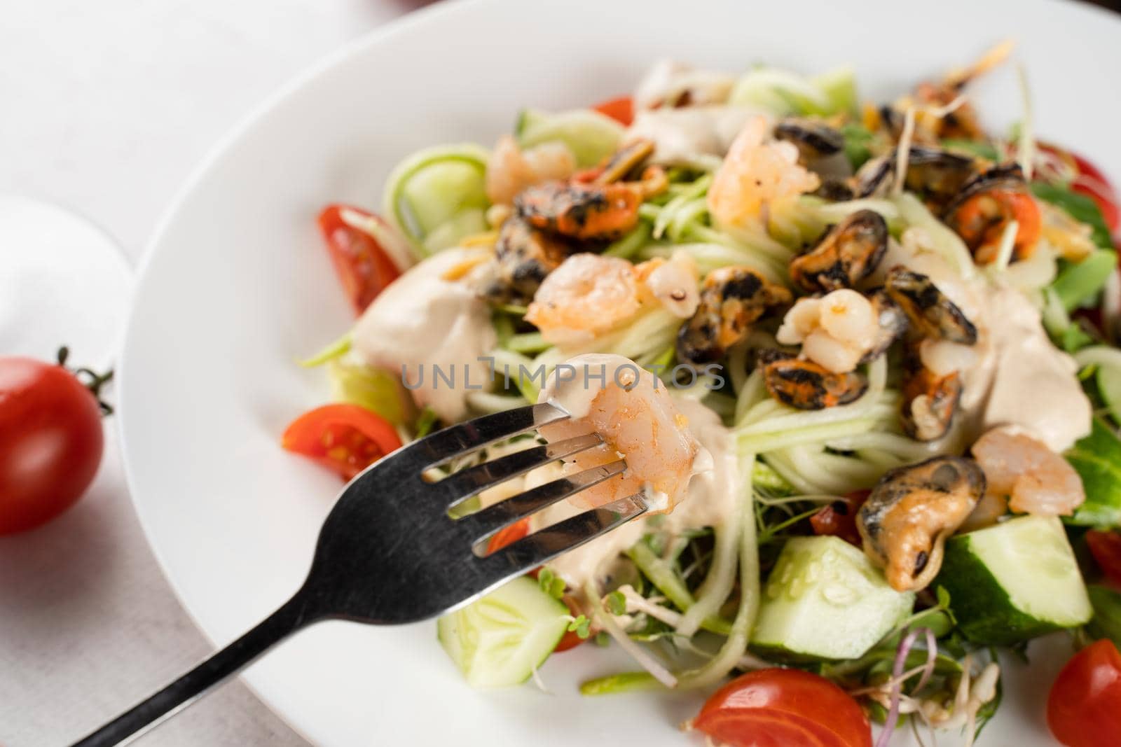 Salad with mussel, shrimp, tomato cherry, cucumber, zucchini pasta, microgreen, yogurt sauce on white plate on light table. by Rabizo