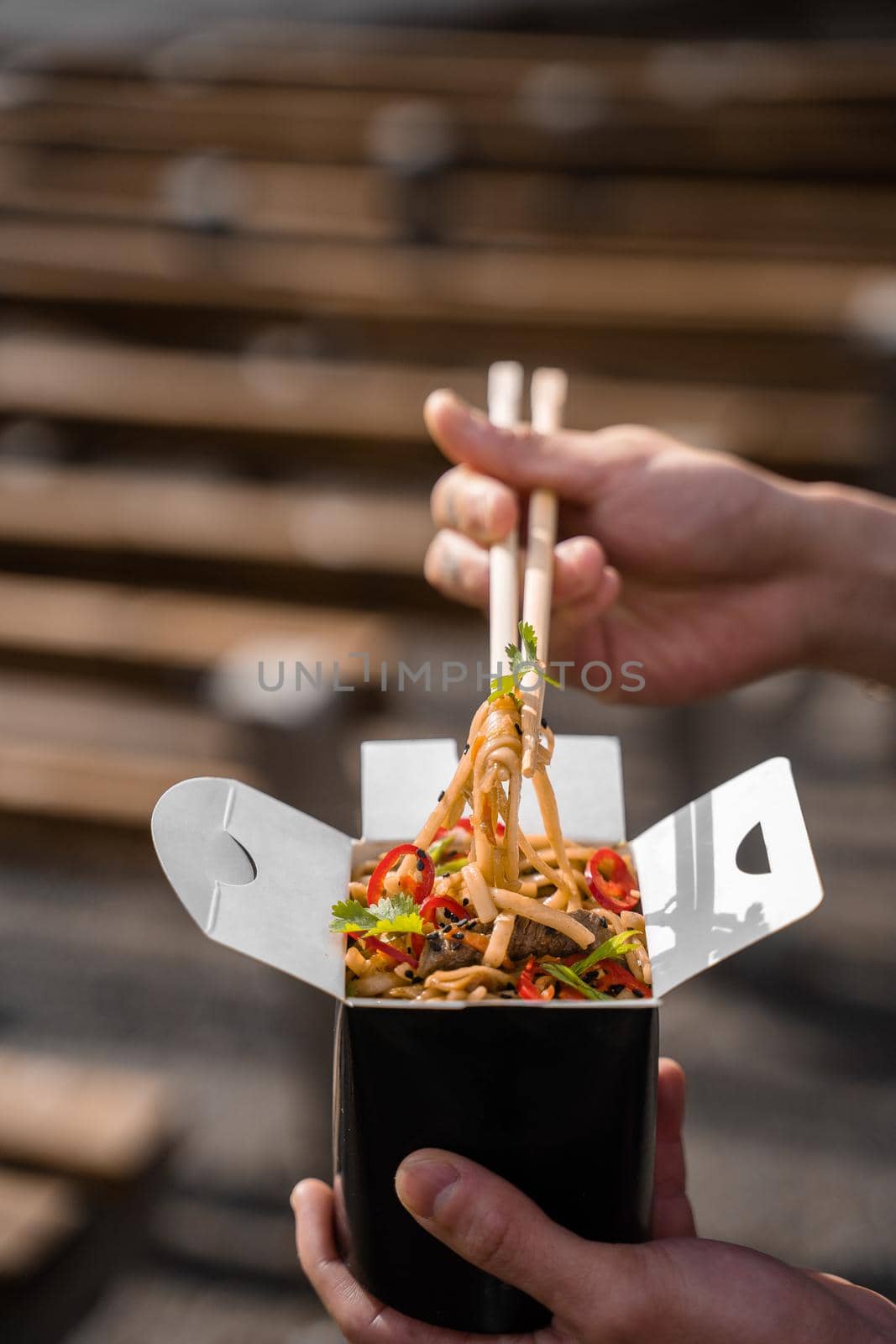 Wok in box in black food container. Holding spicy noodles with chopsticks. Fast food delivery service. Takeaway chinese street meal. by Rabizo