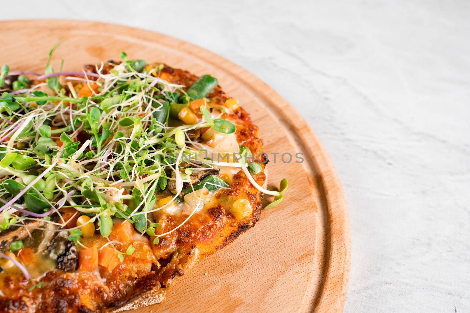 Vegan pinsa romana with mushrooms, asparagus, corn, peas, carrots, cheese and sauce, garnished with microgreens on wooden board. by Rabizo