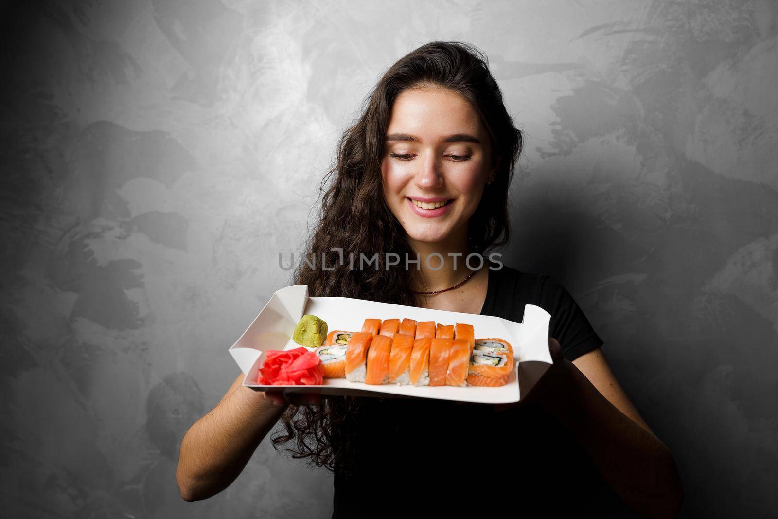 Girl holding philadelphia rolls in a paper box on gray background. Sushi, food delivery