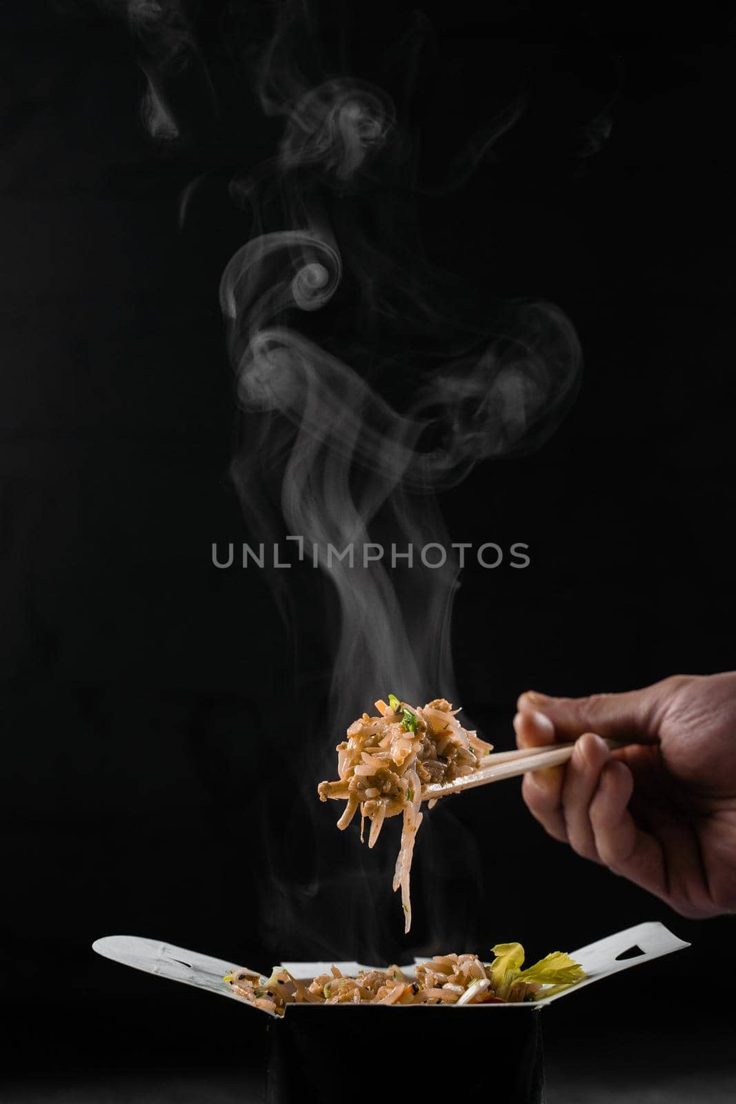 Steaming hot rice in wok box on black background. Holding rice with chinese chopsticks. Asian spicy dish for street restaurant and fast food delivery service