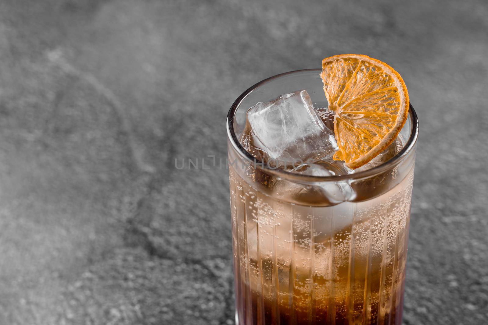 Cocktail in glass with cola, alcohol, ice, decorated dried orange on gray background