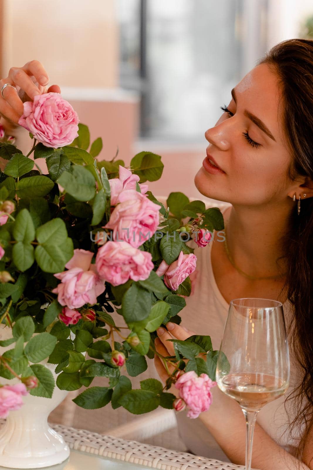 Dreaming woman with glass of alcoholic white wine in cafe in summer terrace and bouquet of roses on the table. by Rabizo