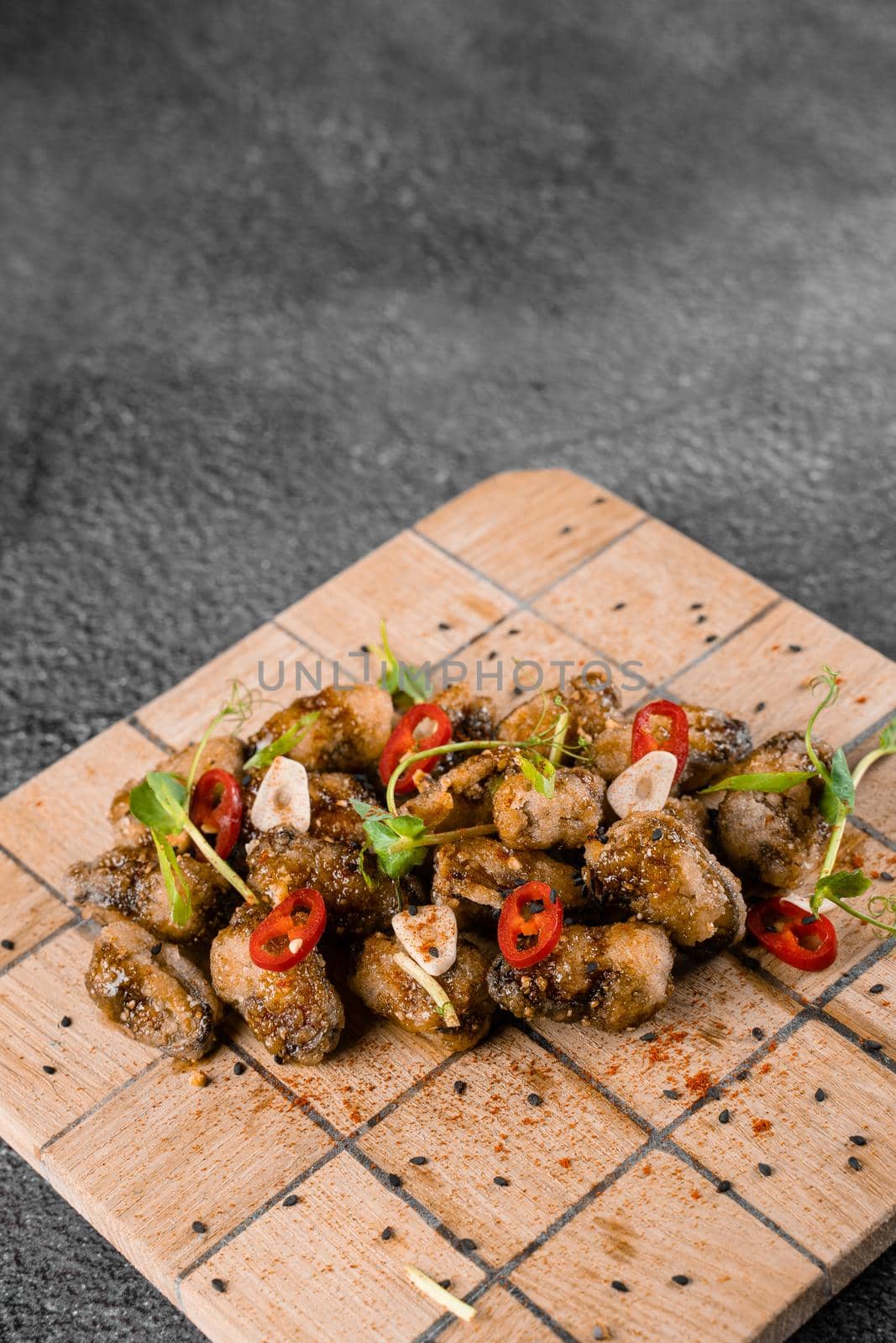 Fried mussels with chili, garlic, sesame, herbs, on square wooden board on gray background