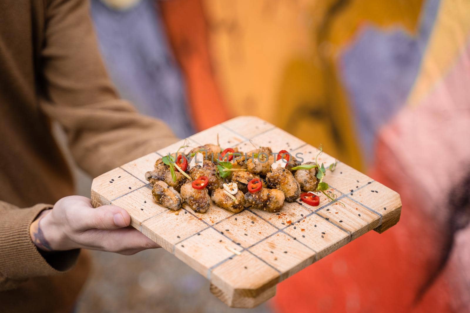 Fried mussels with chili, garlic, sesame, herbs, on square wooden board. Serving the dish by the waiter