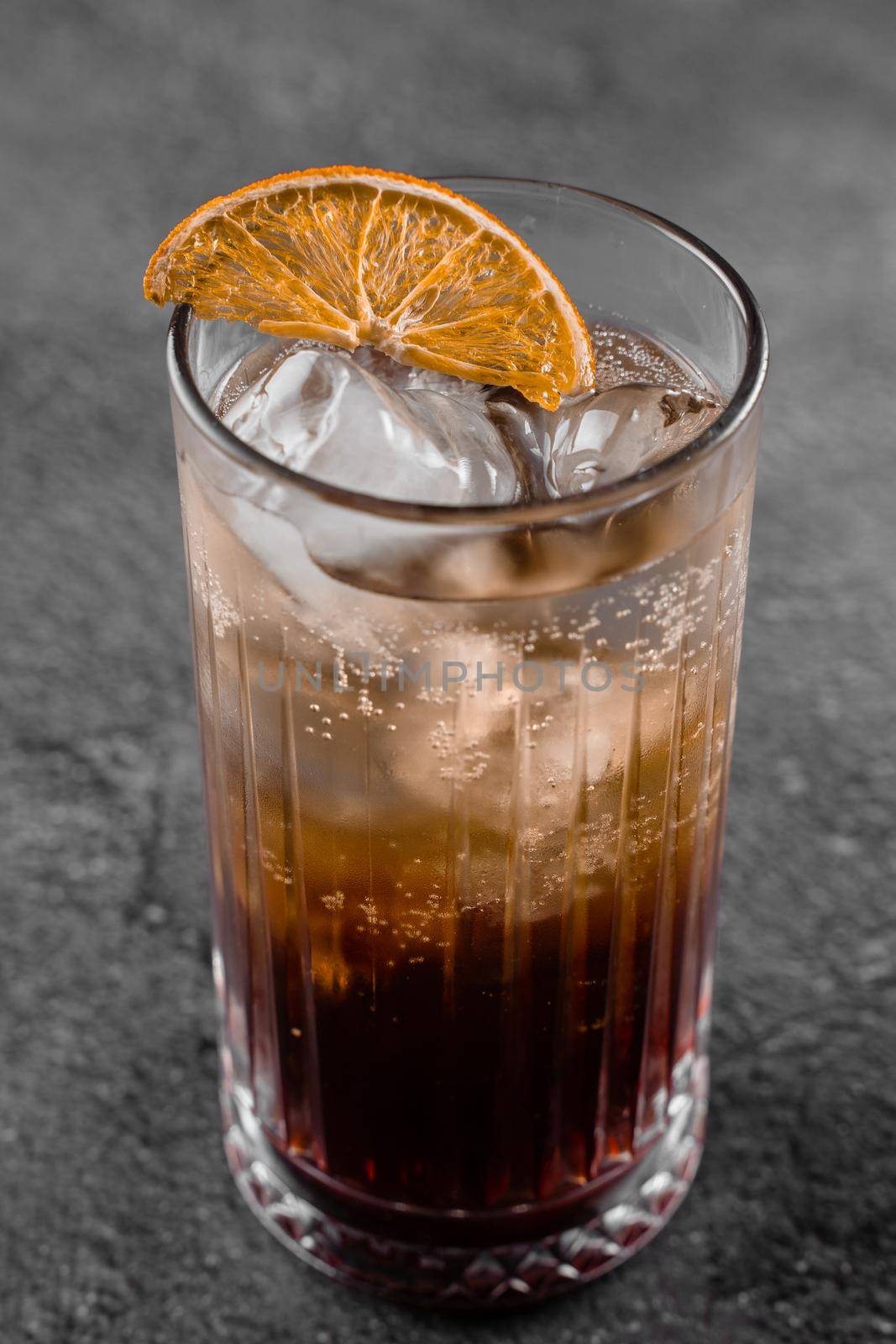 Cocktail in glass with cola, alcohol, ice, decorated dried orange on gray background