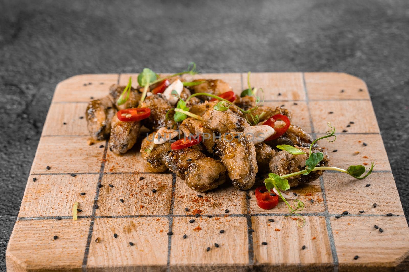 Fried mussels with chili, garlic, sesame, herbs, on square wooden board on gray background