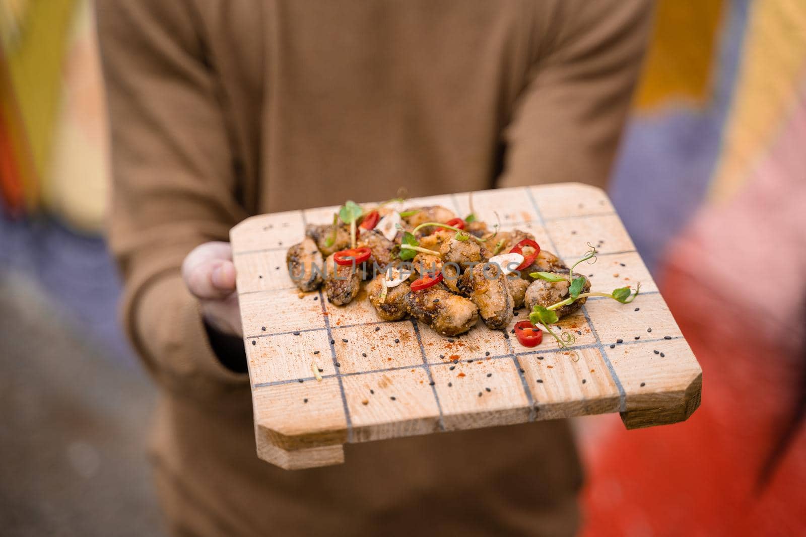 Fried mussels with chili, garlic, sesame, herbs, on square wooden board. Serving the dish by the waiter