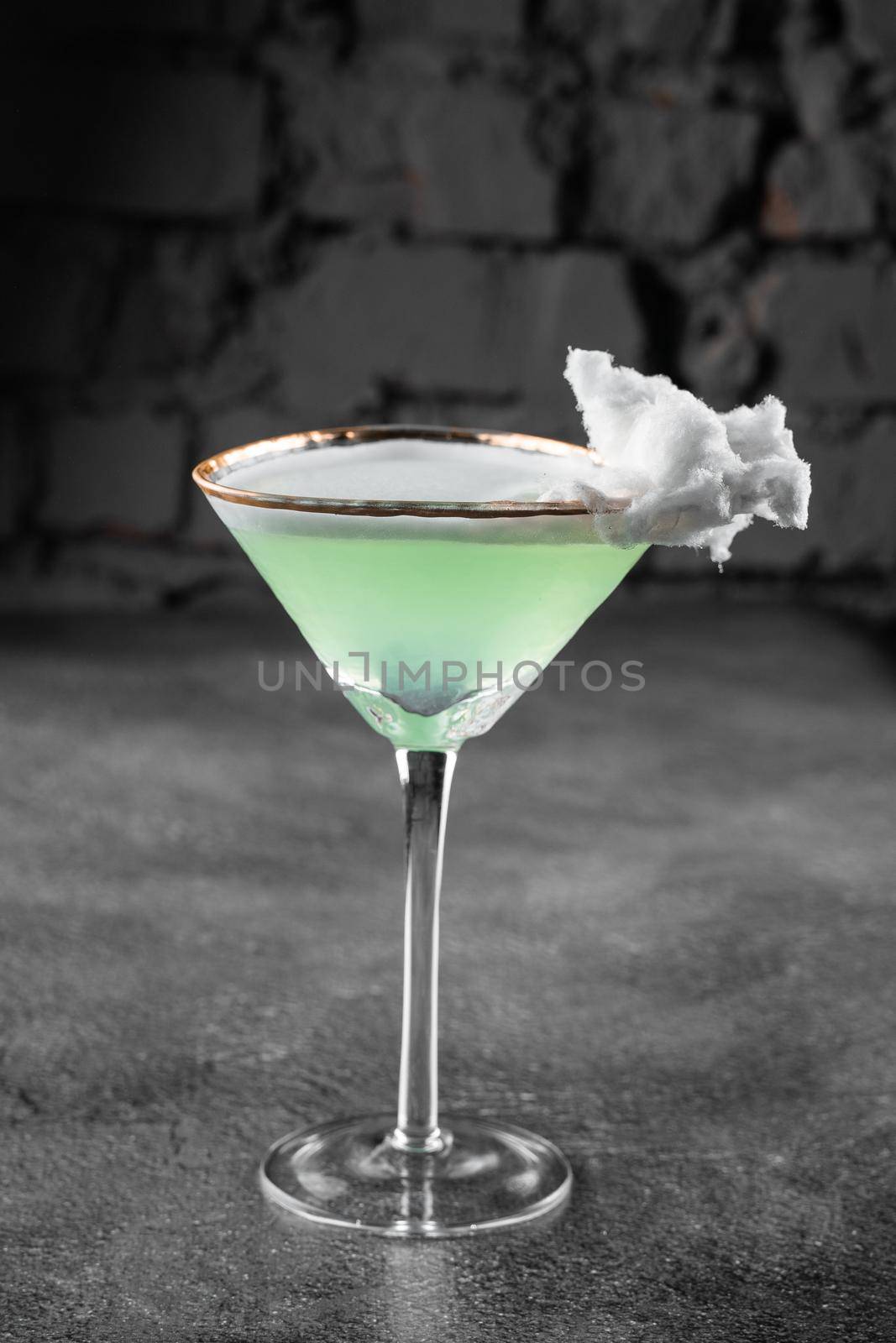 Green alcohol cocktail in a glass decorated with cotton candy on gray background. by Rabizo