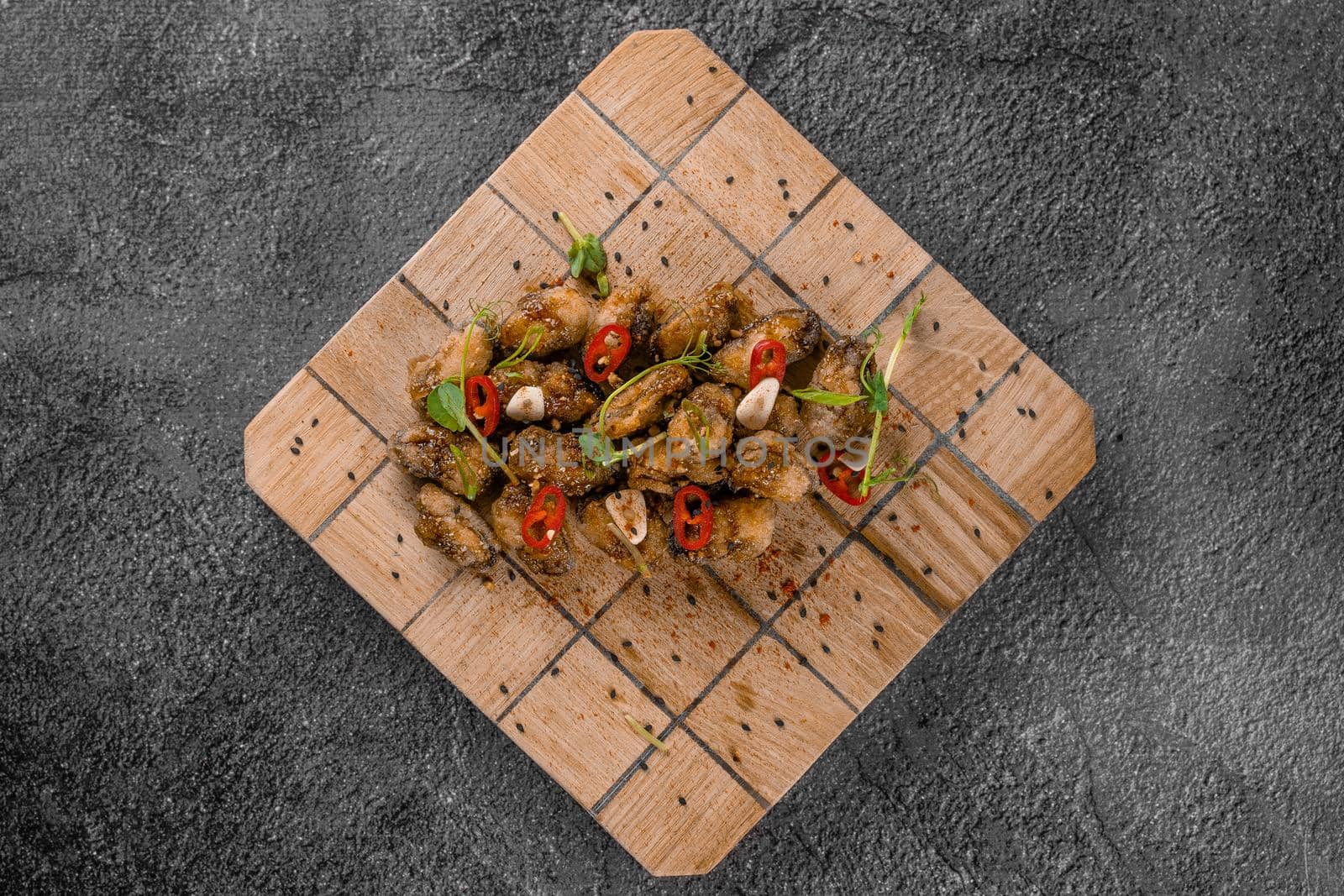 Fried mussels with chili, garlic, sesame, herbs, on square wooden board on gray background. by Rabizo