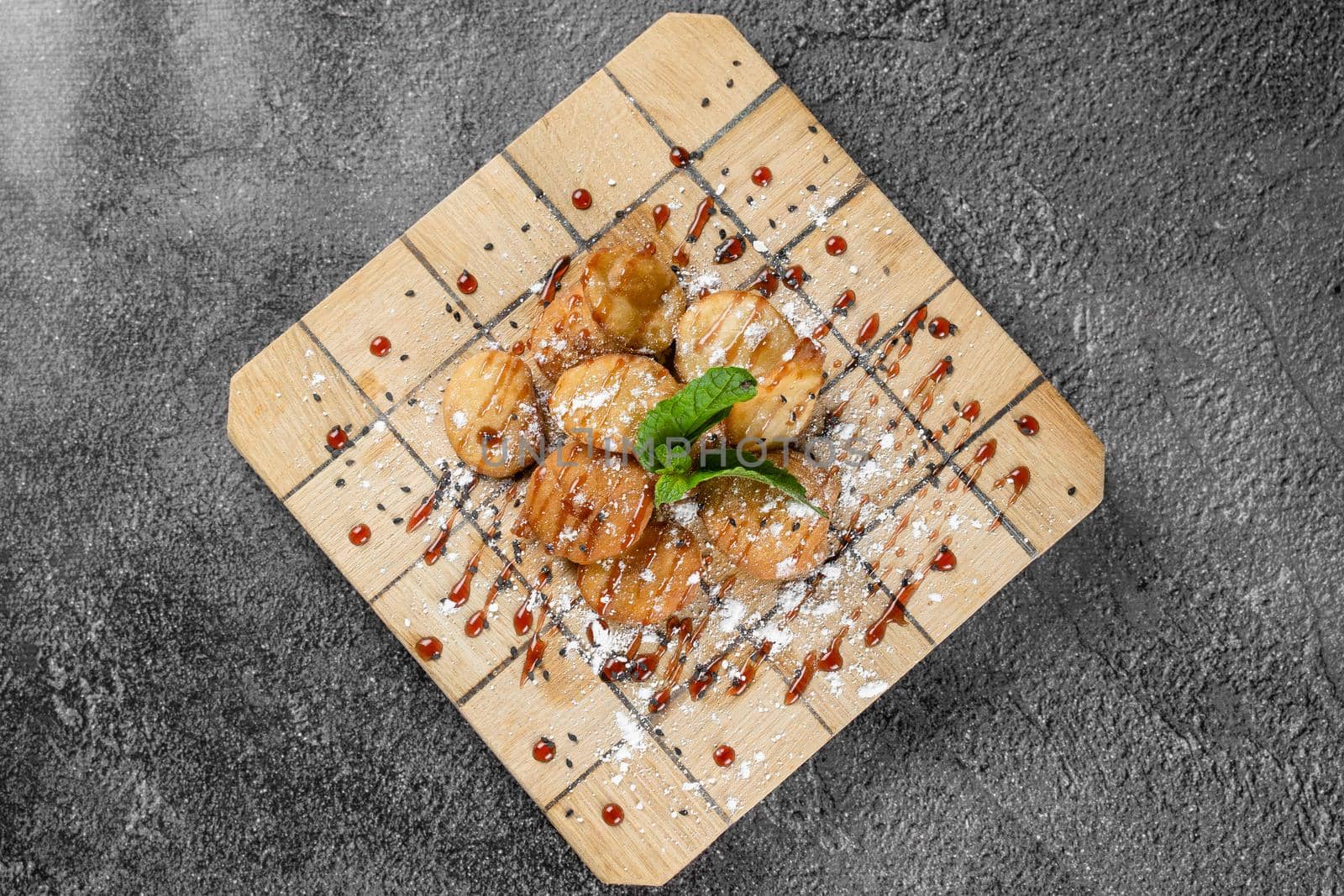 Rice crackers with maple syrup and powdered sugar garnished with mint on square wooden board on gray background. Deep-fried biscuits