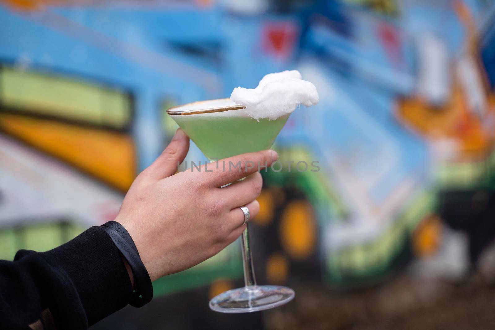 Green alcohol cocktail in glass decorated with cotton candy on color background