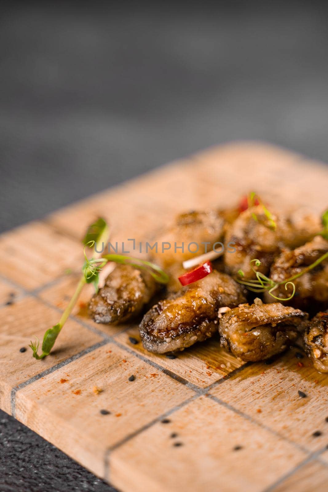 Fried mussels with chili, garlic, sesame, herbs, on square wooden board on gray background