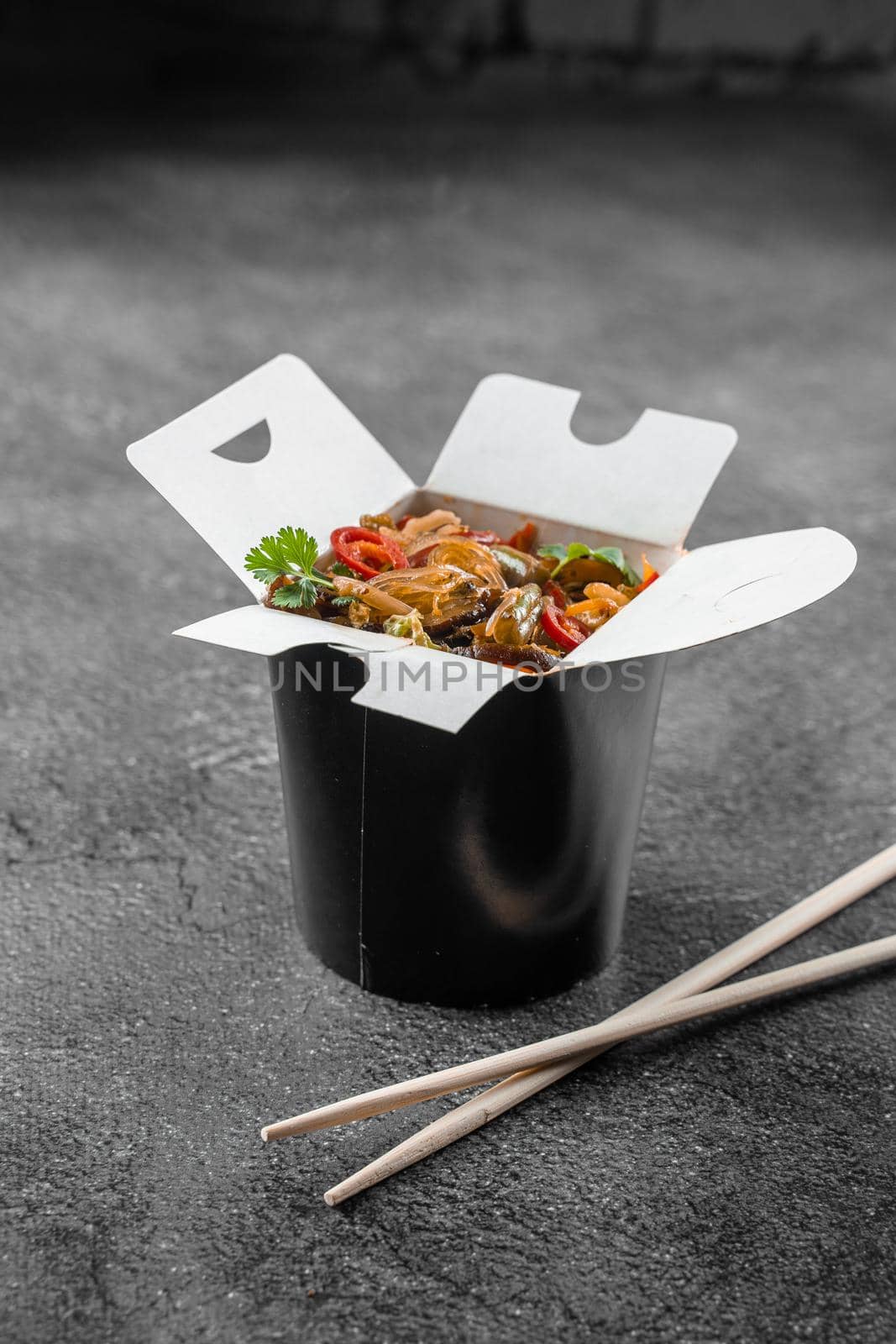 Wok in box rice noodles in black food container. Fast food delivery service. Takeaway chinese street meal